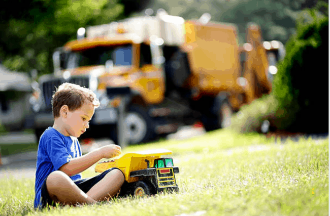 Le garçon est assis par terre et joue avec un camion à benne basculante.